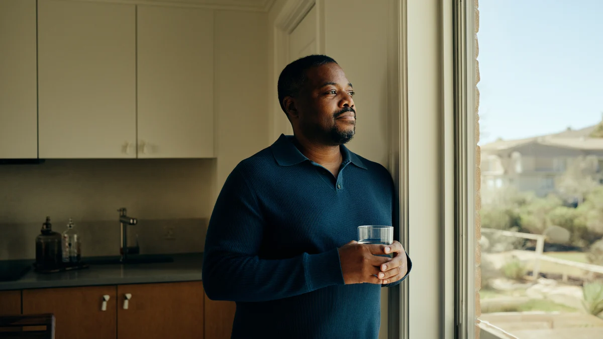 adult holding a glass of water beside a sunlit kitchen window